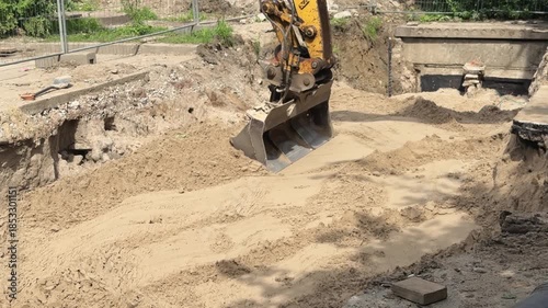 Yellow excavator bucket operates with sand and ground. Industrial machine levels and prepares construction site.