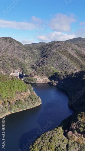 日本のドローン映像　冬の晴れた日に山とダム湖から遠ざかりながら空撮