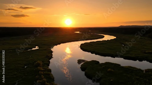 Serene aerial view of a winding river reflecting the warm sunset light through lush green fields