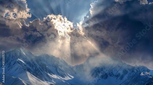 Dramatic sun rays breaking through dark clouds over snow covered mountains