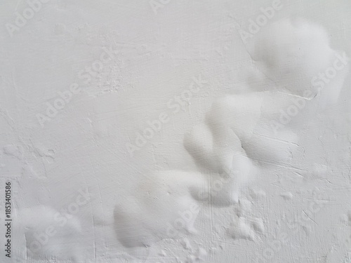 White painted wall with severe bubbling and peeling due to moisture. Close up of water damaged wall surface with large paint blisters. Abstract texture of swollen, damaged white paint and plaster.