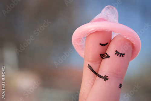 Two fingers with drawn faces hugging under a pink condom hat as a symbol of safe love and protection in romantic relationships