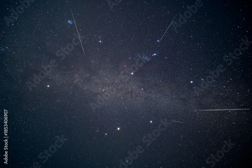 A stunning long exposure of Geminid meteor shower streaks across the Winter Hexagon asterism and a faint Milky Way in a clear dark night sky. Breathtaking astronomical event.