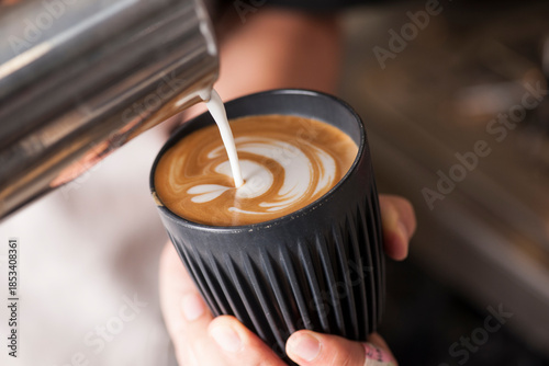 Foto Barista pouring milk to create latte art in a black reusable coffee cup