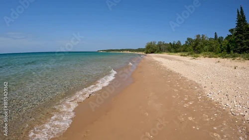 Stunning Natural Beauty on the Sandy Shore of Lake Michigan. Moving backwards along the coast. Waves crash onto the sandy beach with rocks. Wilderness State Park in Northern Michigan, USA.