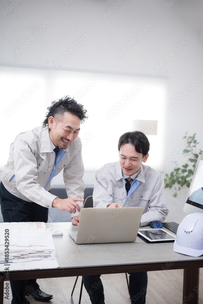 Fototapeta premium パソコンを見ながら笑顔でポシティブに話す作業着のビジネスマン2人 製造業などのdxやit化のイメージ 