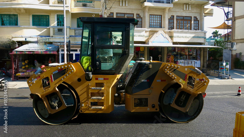 Asphalt road roller. Road roller parked on a city street during daytime. Heavy construction machine with steel drums stands near buildings, showing urban road work and infrastructure maintenance.