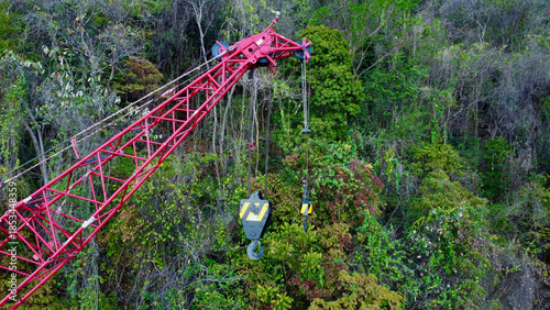 Red construction crane working on a forested hillside.
Heavy lifting equipment stands against dense green woodland.