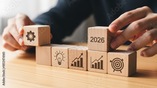 Human hand arranging wooden blocks with business icons and the year 2026
