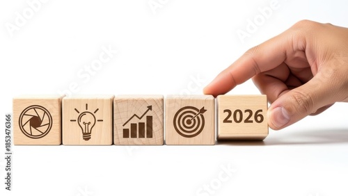 Hand pushing a wooden cube with year 2026 onto a row of business concept blocks