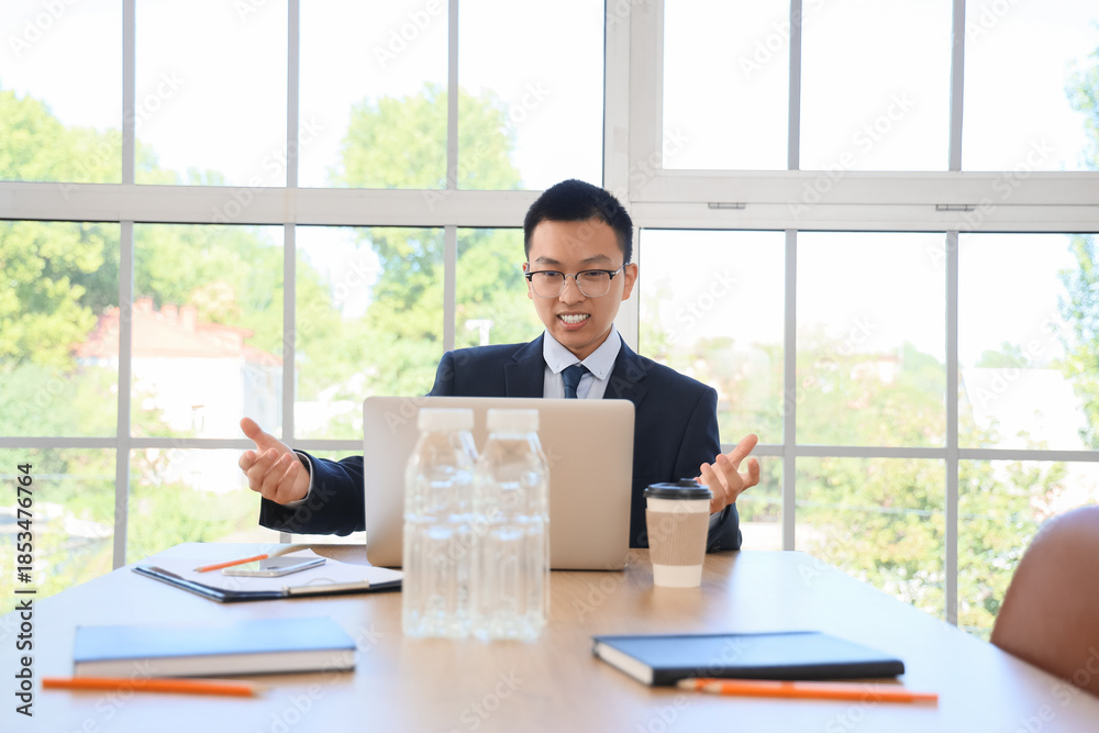 Fototapeta premium Chinese businessman with laptop video chatting at table in office
