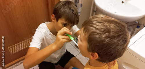Schilderij op canvas Older boy helping younger boy brush teeth in bathroom setting