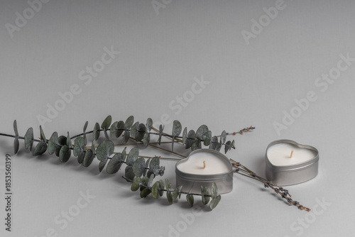 Two heart-shaped candles next to eucalyptus leaves on a gray background.