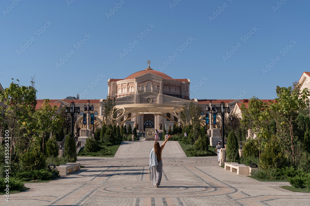 Obraz premium Woman, Church, Garden - Tourist taking a photo in front of a beautiful church in a garden setting.