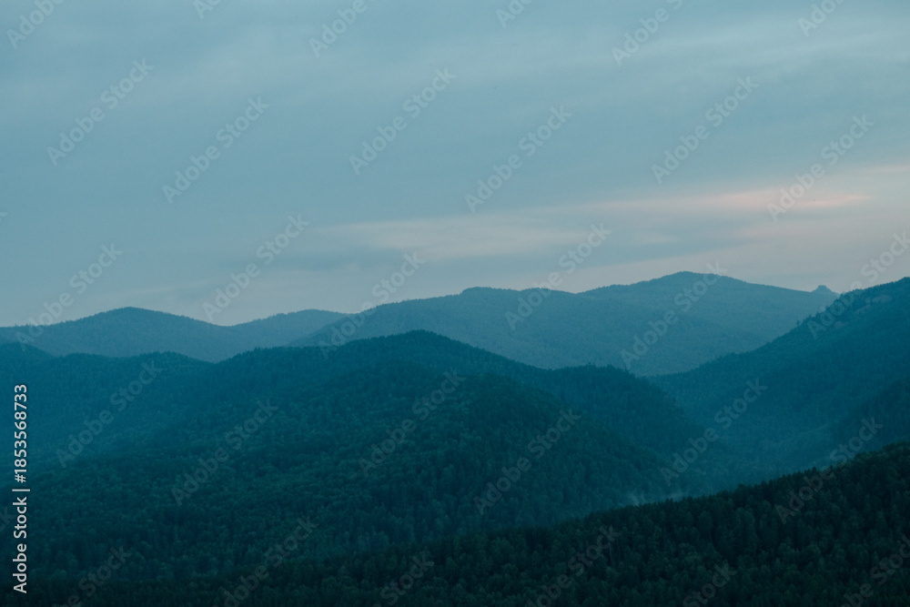 Obraz premium A view of blue distant mountains with wisps of fog after sunset, blue landscape