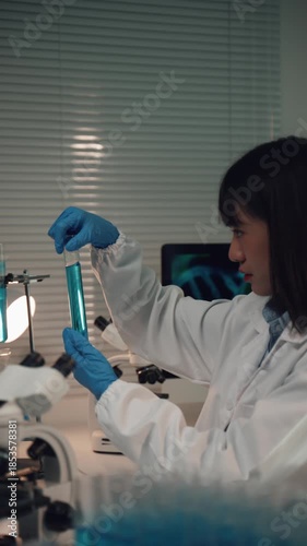 Young Asian female scientist analyzing a sample in a test tube. Concentrated woman developing a new vaccine or drug in a modern laboratory
