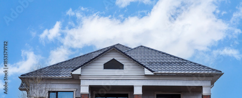 The roof of a house made of gray metal slate against the background of a sky with clouds