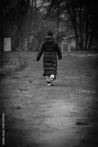 A black and white photograph of a solitary person walking away along a forest path during a quiet winter day.