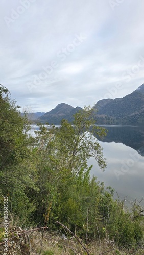 Scenic view of Lago Neltume on a winter day in southern Chile. Calm lake waters surrounded by forested mountains, showcasing pristine nature and a peaceful Patagonian landscape.
