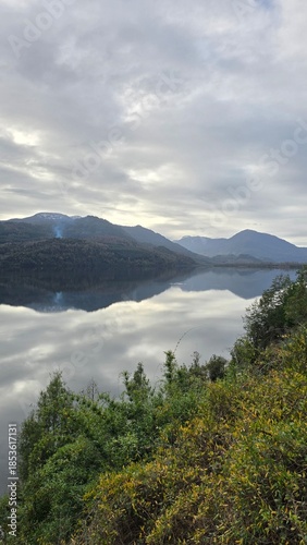 Scenic view of Lago Neltume on a winter day in southern Chile. Calm lake waters surrounded by forested mountains, showcasing pristine nature and a peaceful Patagonian landscape.
