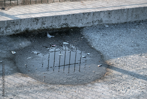 A puddle of water on the asphalt walkway. Concrete pavement.