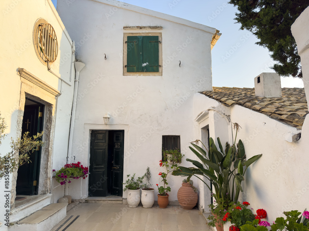 Fototapeta premium Tranquil courtyard of Vlaherna Monastery at Corfu island, Greece. Whitewashed walls, potted flowers, traditional architecture