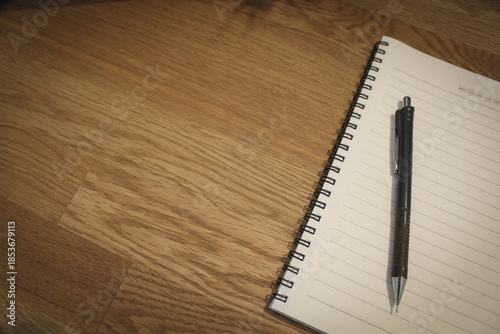 Minimalist workspace concept with spiral notepad, pen, and phone on wooden background.