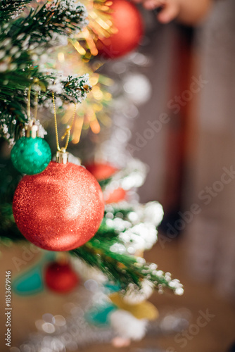 Shiny red and green Christmas tree balls, decorations hanging from dark green branches, create a festive atmosphere.