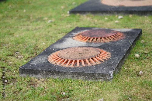 Two orange metal ventilation caps on concrete base for underground septic system or oil interceptor at a gas station service area.