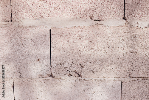 Textured wall of rectangular stone blocks in light beige shades and cement between them.