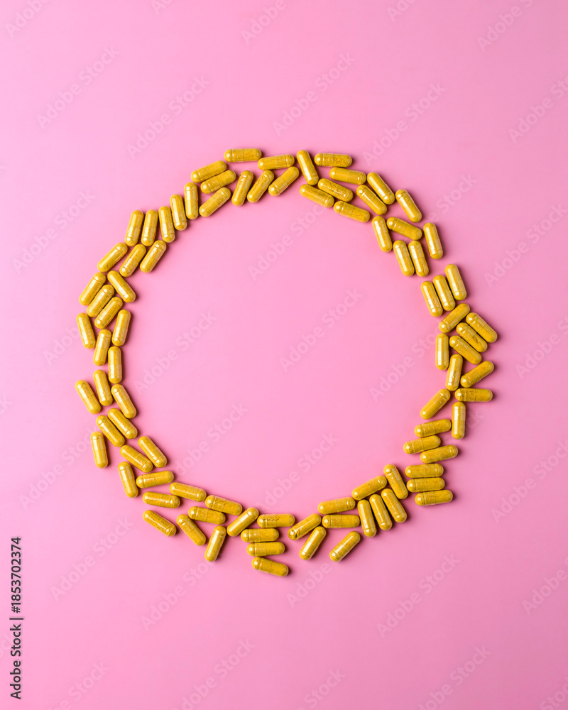 Obraz premium Yellow supplement capsules create circular frame on pink background, clean wellness banner template with central copy space.