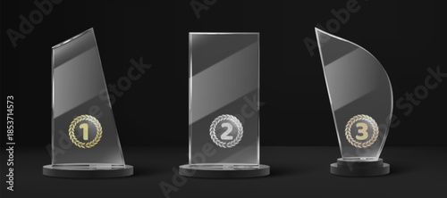 Glass trophy set with golden, silver and bronze laurel wreaths on dark background. Elegant crystal award plates with 1, 2 and 3 place medals with decorative wreath designs for champion recognition.