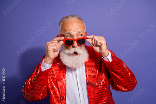 Bearded man in red sequin jacket adjusts red glasses during a vibrant holiday showman performance on a purple background