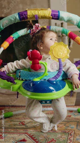 Baby girl standing in colorful activity jumper at home, toddler playing with bright toys indoors, early childhood development and family lifestyle concept