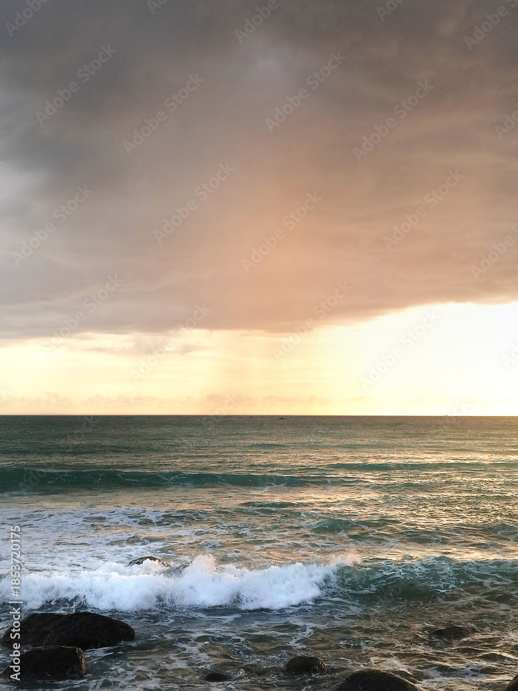 Obraz premium Catching scenic dawn with sunset sky at the beach, with nice waves and low tides, along with summer breeze for a perfect holiday, romantic, and traveling experience.