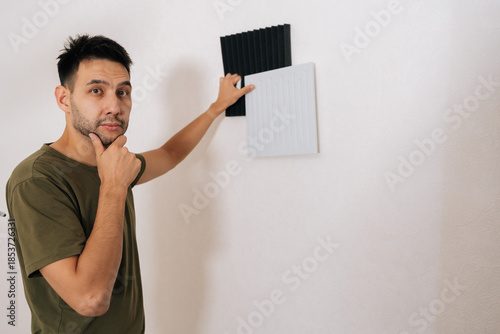 Photos Portrait of thoughtful handyman choosing between two types of soundproof wall panels, comparing designs and textures while installing for acoustic treatment in room, enhancing sound quality
