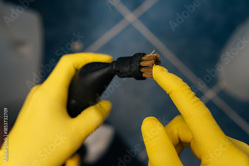 Photography Close-up hands in yellow protective gloves holding checking steam cleaner with brush attachment, preparing to clean bathroom tiles for hygiene, sanitation and household chores