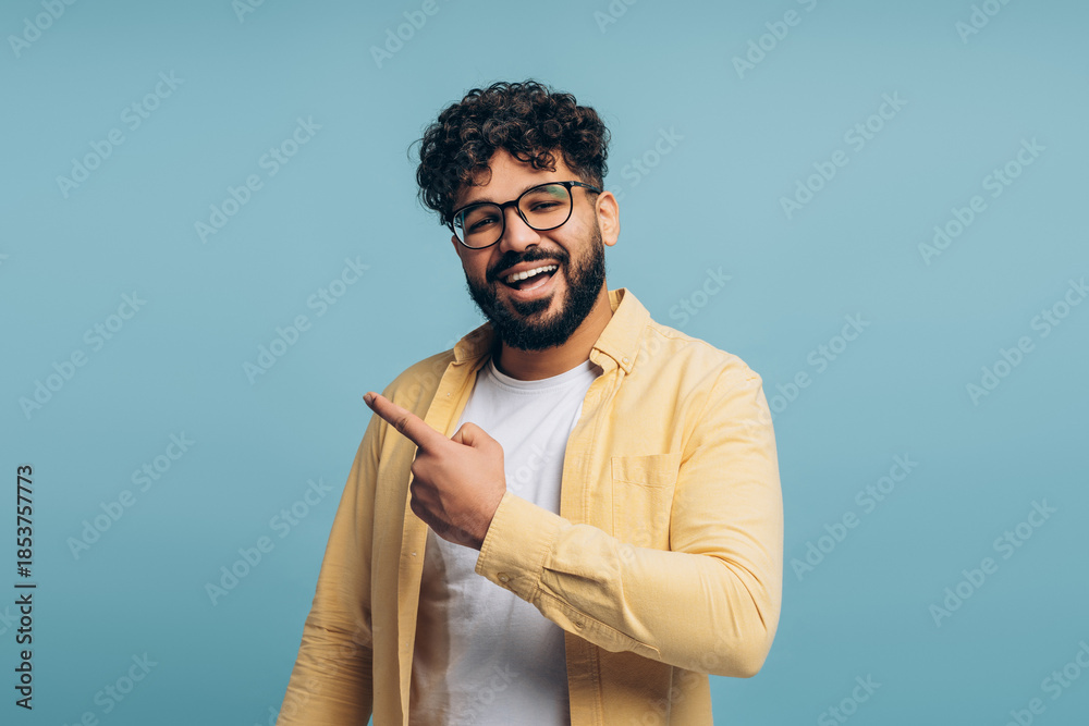 Obraz premium Smiling man wearing stylish eyeglasses pointing finger on copy space isolated on blue background