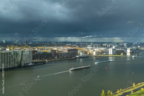 Aerial view of barges glide along the shimmering water, reflecting the steely sky above the cityscape of Amsterdam, North Holland, Netherlands.