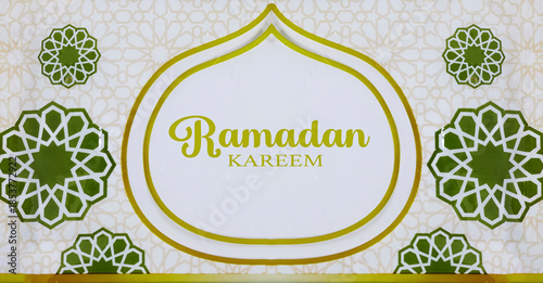 decorative Ramadan banner featuring the text 'Ramadan Kareem' in gold with green geometric rosettes on a soft patterned background, evoking Islamic art