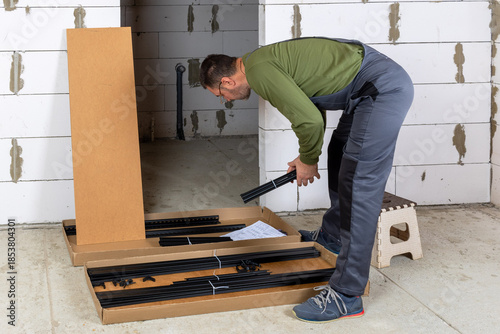 Quadro em tela A middle-aged white man in glasses carefully assembles a metal shelving unit usi