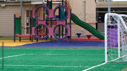 A colorful playground area on an Australian primary school campus featuring climbing frames, slides, and soft-fall safety surfacing beside a small soccer goal. Outdoor play, physical development.