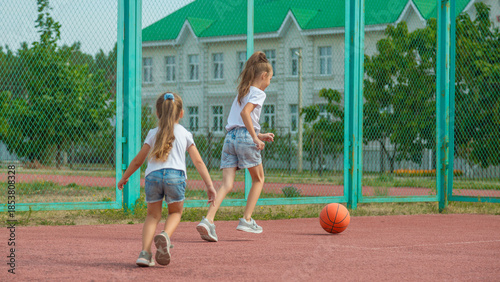 Εκτύπωση καμβά Girl and her younger sister, play basketball on modern basketball court under open sky