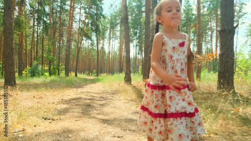 Caucasian child girl walking at a sunny forest. Kid feels positive while having fun in sunny green park. Brunette babe enjoying her vacation spend the weekend in the fresh air