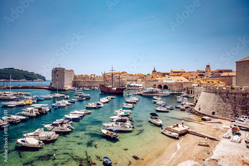 View of a serene harbor filled with boats, medieval stone walls, and historic buildings basking under a clear sky, Dubrovnik, Dubrovnik-Neretva County, Croatia.