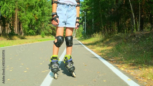 Child girl in casual clothes roller skating on road in forest on sunny summer day.