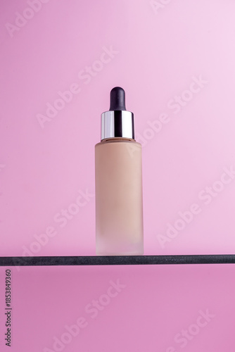 Frosted glass bottle of liquid foundation with dropper on a shelf against a pink background