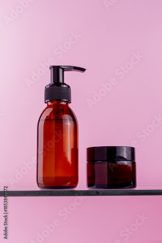 Amber glass bottles with black pumps and lids on a shelf against a pink background