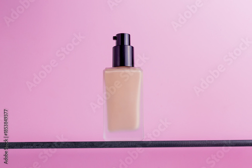 Luxury foundation bottle with pump dispenser on a minimalist shelf against pink background