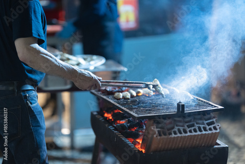 Person grilling street food on outdoor charcoal barbecue